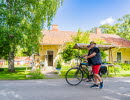 2 bicyclists that are walking in the street with a yellow house in the background