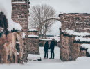 Snowy landscape. Two people stand and look up at an arch in the ruins of the monastery church in Gudhem.