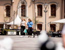 Två tjejer går över torget med shoppingkassar och en svart hund.