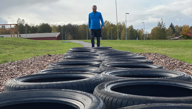 Ett man i blått står vid ett hinder av bildäck på en rad, på friluftsområdet lassalyckan i Ulricehamn. 