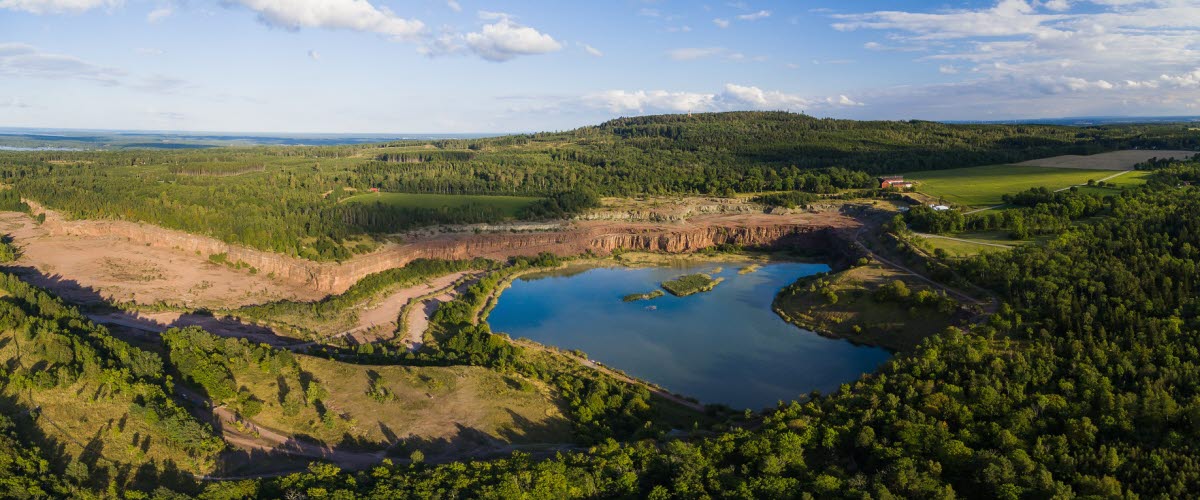 Flygbild över Stora Stenbrottet på Kinnekulle. Sjö i mitten omgiven av berg och skog.