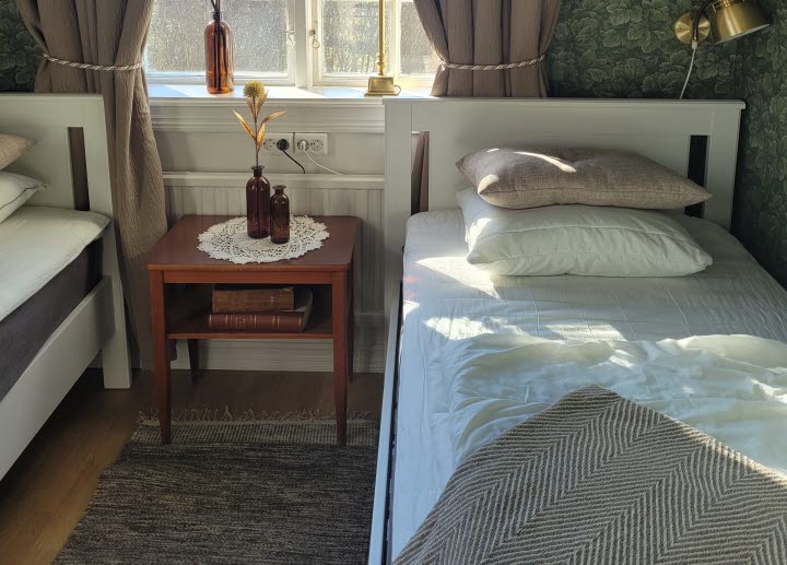 Two beds in a room. Between the beds there is a small nightstand with two brown glass vases.