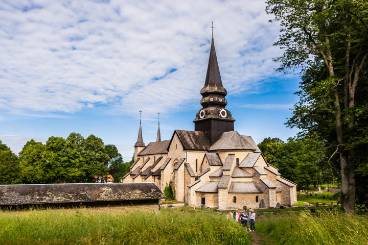 Varnhems klosterkyrka. I förgrunden syns vandrare gå mot den imponerande stenkyrkan.