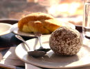 En kaffekopp med bulle och en chokladboll på ett fat med två skedar