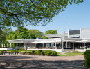 A hotel and their outdoor terrace, in front of is a large gravel field.