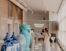 A woman in a bright dress walks around inside a museum where large porcelain pieces are lined up along one wall.
