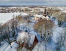 Ett drönarfoto av en stor stenkyrka och en träbyggnad. På marken ligger ett tunt lager snö.