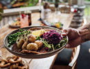 A hand with a tattoo is holding a plate with food. 