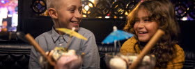 A boy and a girl sittning in a restaurant with two desserts in front of them. 