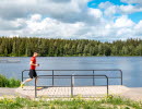 Man som springer utmed ett motionsspår, över en bred träbro, bakom breder sjön Hållsdammen ut sig och på andra sidan om den syns skogen.