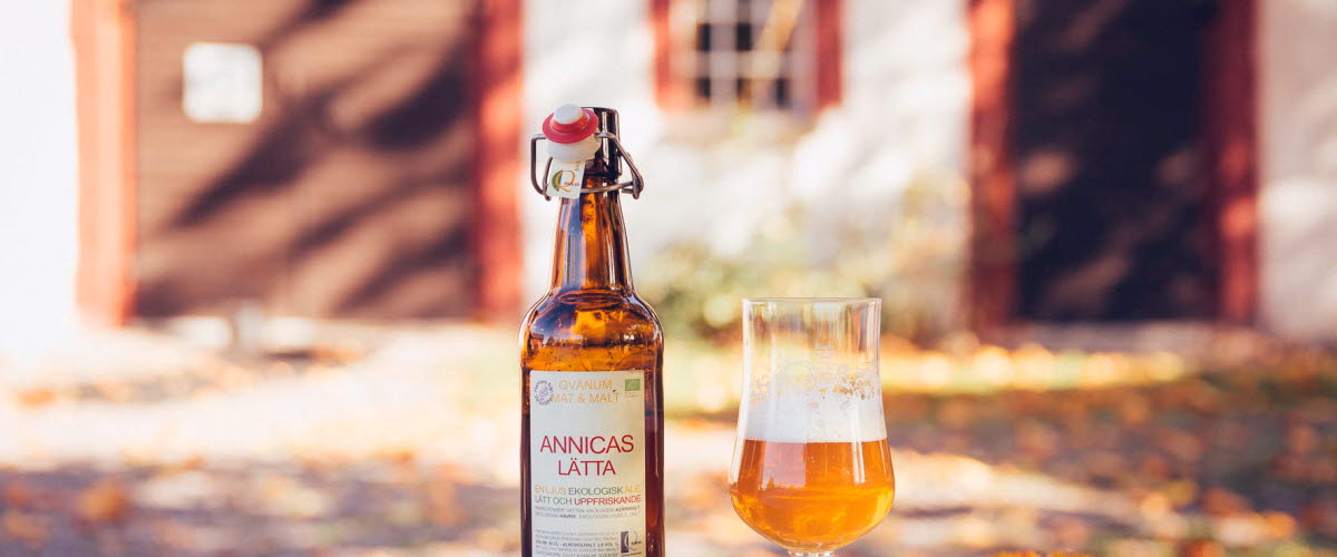 A product image of a beer and a poured glass in front of a well-kept barn.