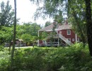 A red larger house with white knots, stairs and porches located in a lush area.