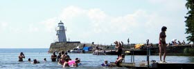 Several people bathing from a bathing jetty. In the background is a lighthouse on a pier. It is a beautiful summer day.