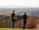 Två personer i färgglada kläder vandrar bort från kameran med en vindunderlig utsikt över Vallebygden. 