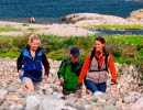 Three people are hiking across a cobblestone field at North Koster. 