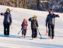 A family with two adults and two children walks in the snow and carries their skis.