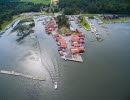 Aerial view over Spikens fishing harbour. Two lanes of red houses along the wharf surrounded by water. A boat is leaving the harbour creating waves behind.