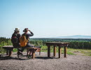 Two women sitting on a bench looking out over the landscape with Kinnekulle at the horizon. 