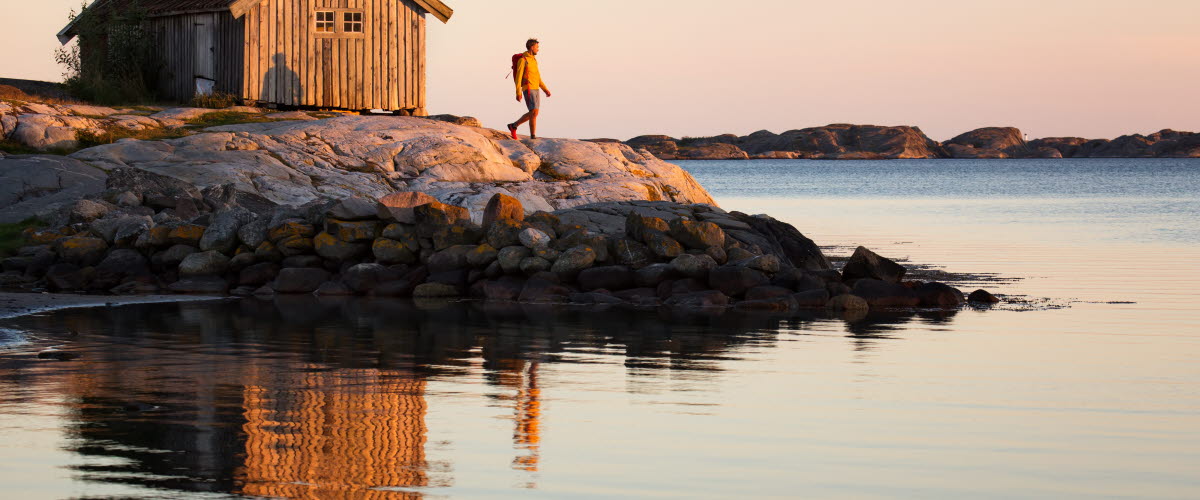 Vandrande man vid sjöbod i solnedgången