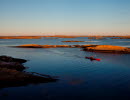 A red kayak is paddeling next to an island at dusk. 